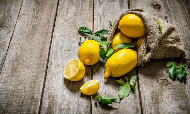 Limoni freschi in una vecchia borsa con foglie. Sullo sfondo di legno.