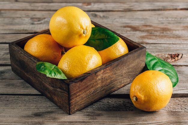 Limoni freschi in una vecchia scatola con foglie su fondo di legno rustico