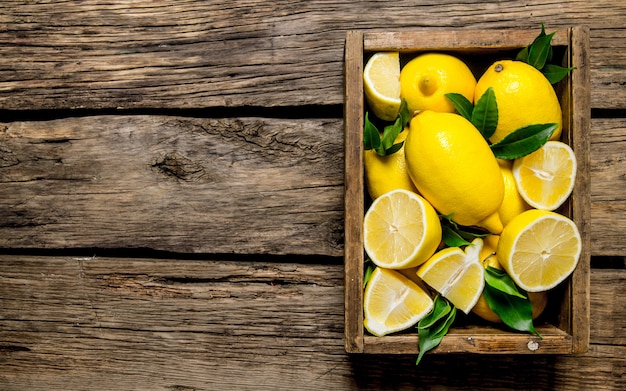 Limoni freschi in una vecchia scatola con foglie sulla tavola di legno. Vista dall'alto