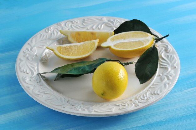 Limoni gialli freschi con le foglie su un piatto su fondo blu