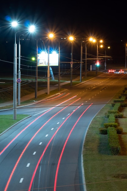 Linee di luce della città notturna da automobili automobili in autostrada con movimento sfocato Vista sulla strada della città moderna di notte Molta luce dai fari delle auto banner pubblicitari e luci notturne