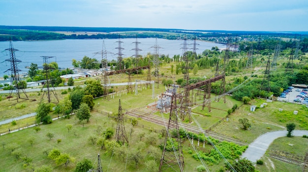 Linee di trasmissione elettriche su campi agricoli verdi vicino al fiume. Linee elettriche nel bellissimo paesaggio della natura. Vista aerea