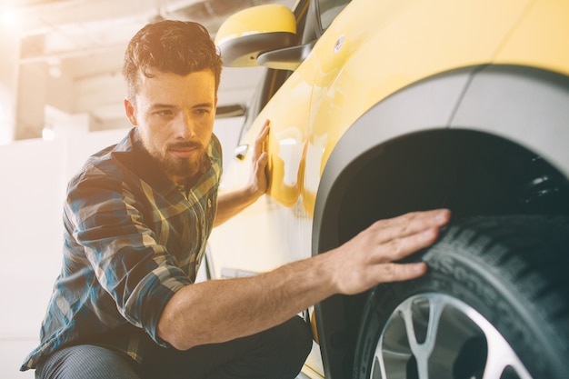 Linee perfette. Il giovane uomo barbuto dai capelli scuri esamina l'auto presso la concessionaria e fa la sua scelta. Ritratto orizzontale di un giovane ragazzo in macchina. Sta pensando se dovrebbe comprarlo.