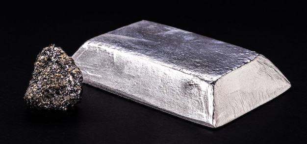 Lingotto o barra di zinco isolato accanto alla pepita di zinco grezzo su sfondo nero isolato, metallo utilizzato nella produzione di leghe e acciaio