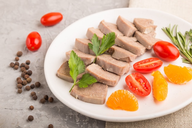 Lingua di maiale bollita con pomodori ed erbe su una superficie di cemento grigia. Vista laterale, messa a fuoco selettiva.