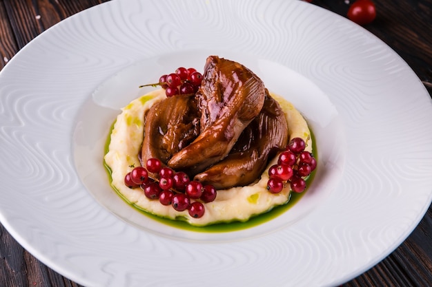 Lingue di agnello in umido con ribes rosso su un piatto bianco.