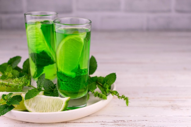 Liquore alla menta con lime e foglie di menta su un tavolo di legno bianco. Spazio per la copia.