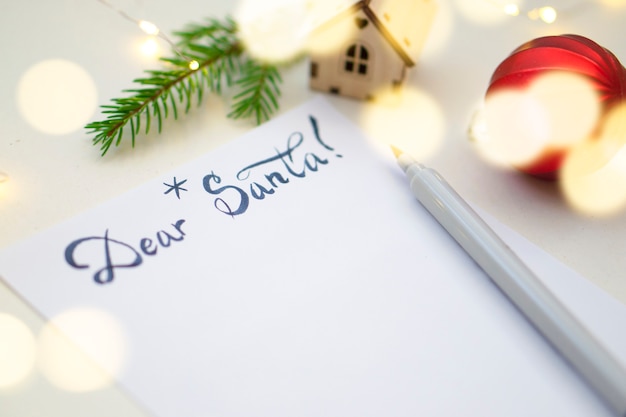 Lista dei desideri di Natale 2022 o lettera a Babbo Natale su uno sfondo di carta di colore chiaro. Decorazione festiva, ghirlanda di Natale, ramo di albero di Natale. Disposizione piatta. Vista dall'alto.