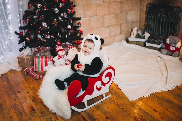 Little boy baby sitting accanto all'albero di Natale decorato con doni e regali