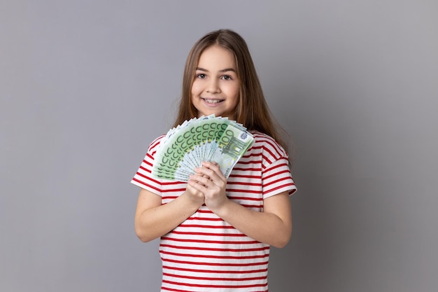 Llittle ragazza che indossa tenendo a ventaglio di banconote in euro che mostra un sacco di soldi e guardando la fotocamera