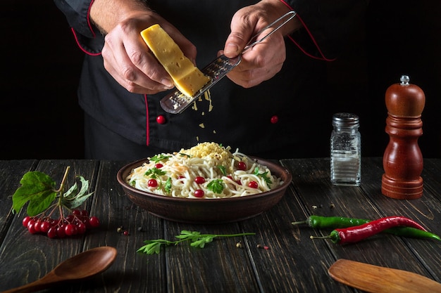 Lo chef aggiunge formaggio su spaghetti con verdure in un piatto Menu o ricetta per un delizioso pranzo per un hotel o un ristorante