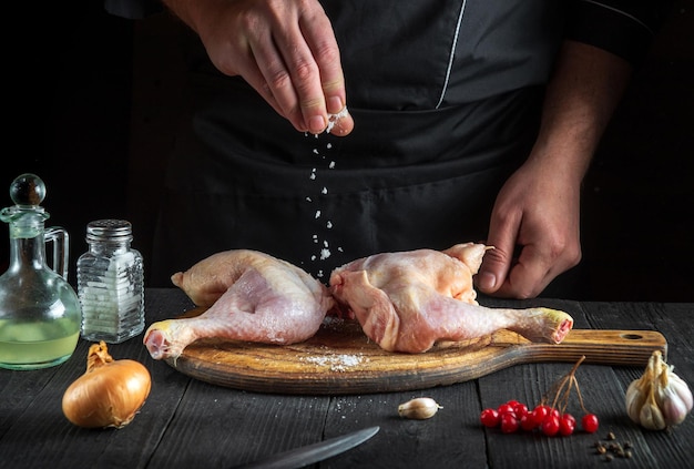 Lo chef aggiunge sale alle cosce di pollo in cucina