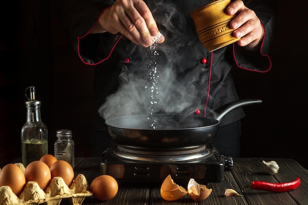 Lo chef aggiunge sale durante la cottura delle uova o una frittata in padella Ambiente di lavoro sul tavolo della cucina