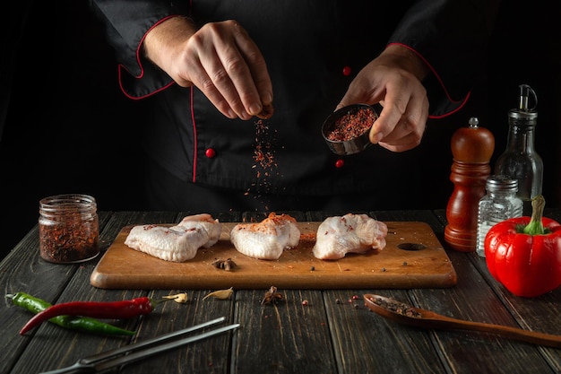 Lo chef aggiunge spezie aromatiche alle ali di pollo crude Cucinare la pepita di pollo nella cucina del ristorante