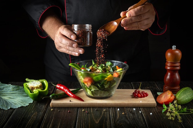 Lo chef aggiunge un condimento aromatico al cibo vegetariano Cucinando deliziose insalate con le mani del cuoco in cucina Idea di menu per un hotel o un ristorante