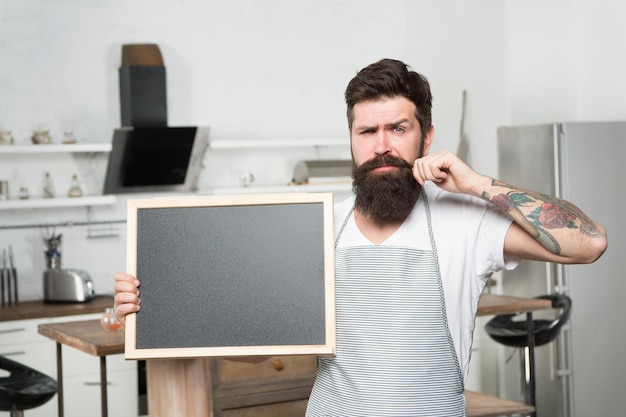 Lo chef brutale dell'uomo con la barba tiene una scheda vuota per il menu dello spazio di copia