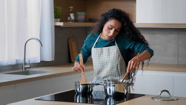 Lo chef casalingo riccio attraente mamma araba occupata indossa il grembiule che prepara la colazione nella cucina di casa