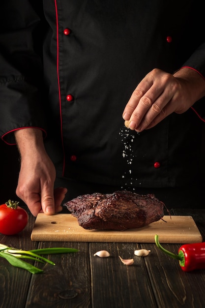 Lo chef cosparge di sale la carne di manzo al forno Ambiente di lavoro sul tavolo della cucina Cucina asiatica