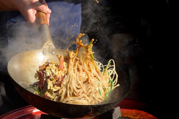 Lo chef cucina il wok cinese di noodle al festival del cibo di strada