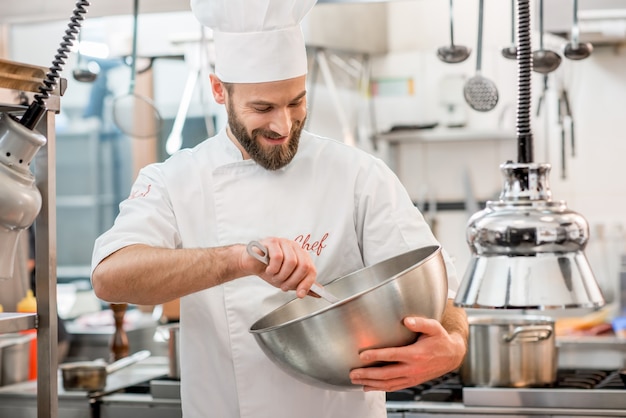 Lo chef cucina in uniforme mescolando insalata nel recipiente di metallo presso la cucina del ristorante