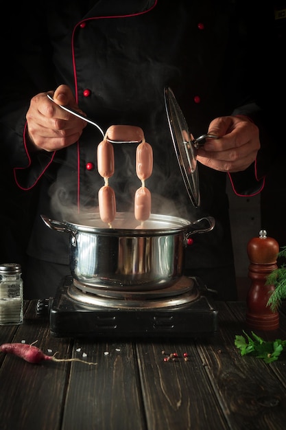 Lo chef cucina salsiccia viennese in una casseruola Ambiente di lavoro in cucina Deliziosa colazione o cena