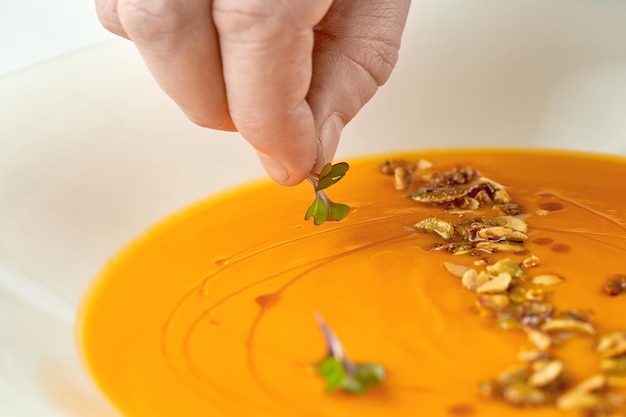 Lo chef decora la zuppa di crema di zucca in un piatto bianco