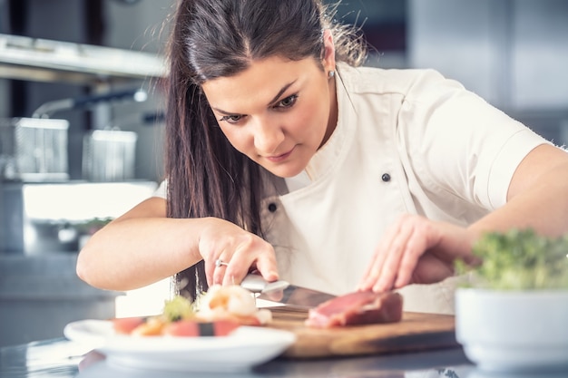 Lo chef di sushi femminile professionista taglia il tonno in una cucina professionale.