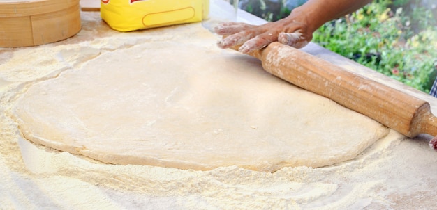 Lo chef donna stende la pasta lievitata con un mattarello sul tavolo. Copia spazio. Cucinare all'aperto. Master Class sulla preparazione di ciambelle dolci.