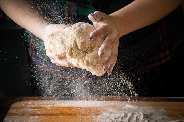 Lo chef femminile impasta la pasta della pizza su una tavola di legno La farina vola su uno sfondo scuro