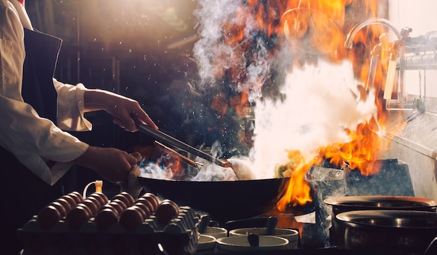 Lo chef friggere impegnato a cucinare in cucina. Lo chef frigge il cibo in una padella, affumica e schizza la salsa in cucina.