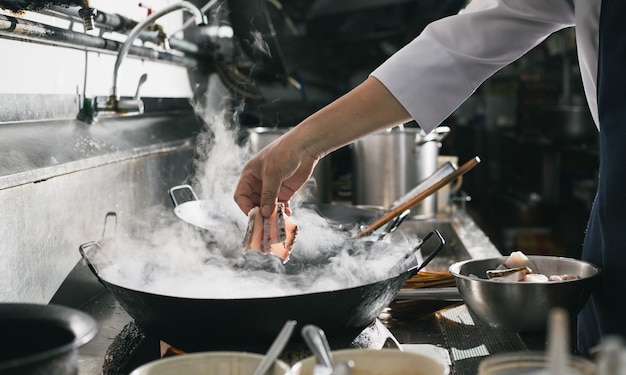 Lo chef friggere impegnato a cucinare in cucina. Lo chef frigge il cibo in una padella, affumica e schizza la salsa in cucina.