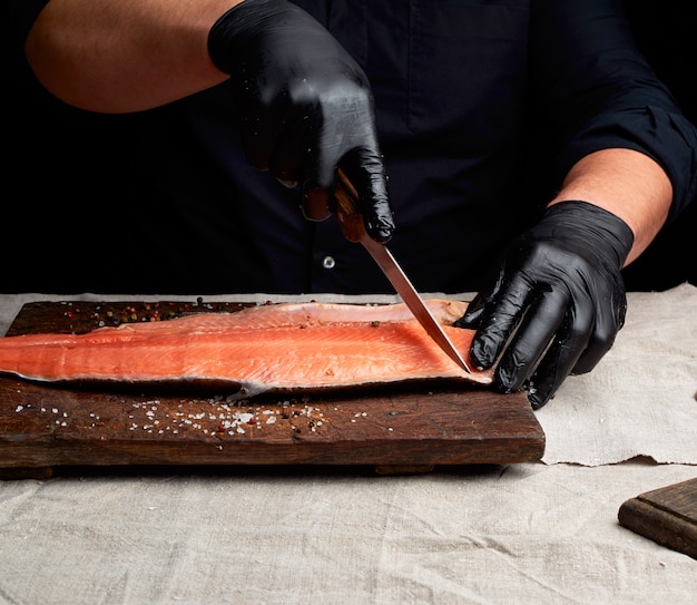 Lo chef in abiti neri e guanti in lattice nero taglia a pezzi il filetto di salmone fresco