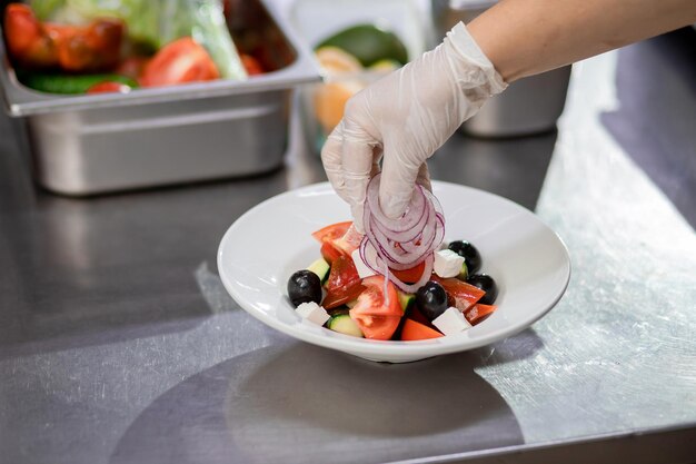 Lo chef in cucina impone cipolle fresche tritate e prepara un'insalata greca Concetto di insalata vegetariana in ammollo