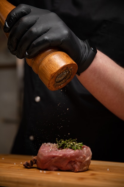 Lo chef in guanti neri marina la bistecca in cucina