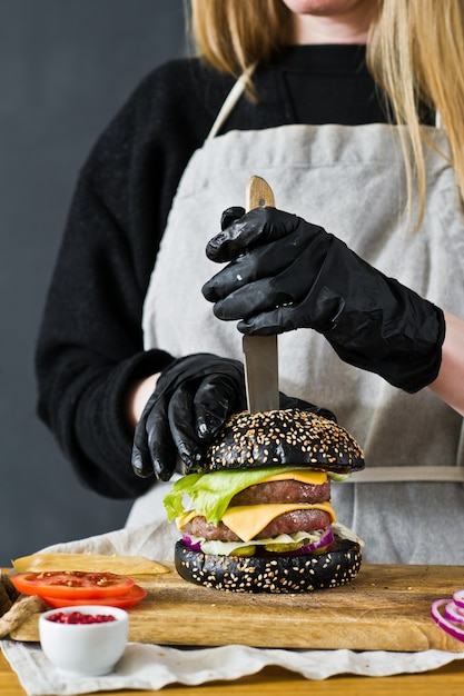 Lo chef infila un coltello nel Burger. Il concetto di cucinare cheeseburger nero. Ricetta hamburger fatta in casa.