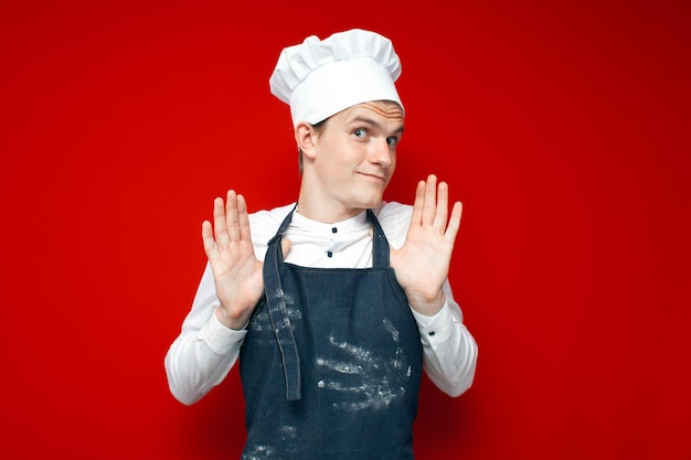 Lo chef insicuro in uniforme scrolla le mani su sfondo rosso isolato lavoratore di cucina in imbarazzo