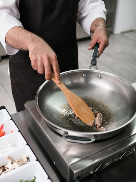 Lo chef lavora presso la cucina del ristorante. cuoco maschio sta preparando un pasto in padella. Stile di vita professionale di successo