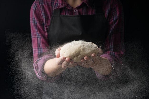 Lo chef mantiene l'impasto e versa la farina su uno sfondo scuro Il concetto di nutrizione