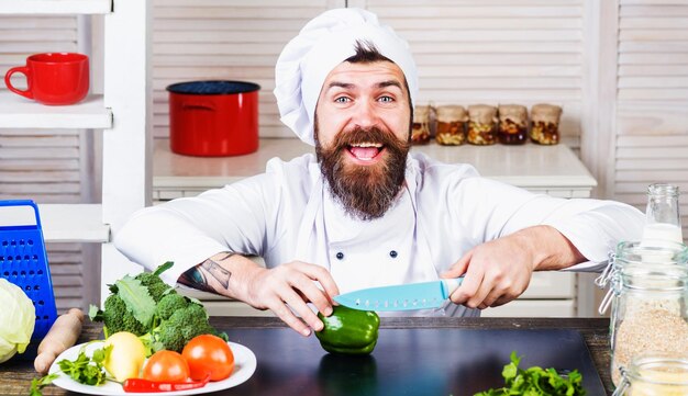 Lo chef maschio in uniforme bianca taglia il pepe con il coltello che cucina insalata di verdure dieta cibo sano