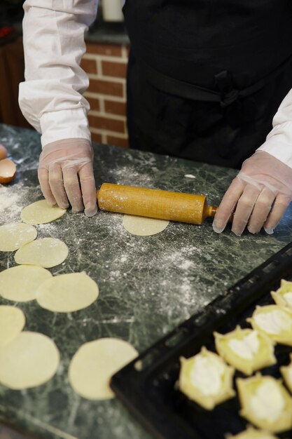 Lo chef maschio usa gli ingredienti per preparare i prodotti a base di farina sul tavolo della cucina