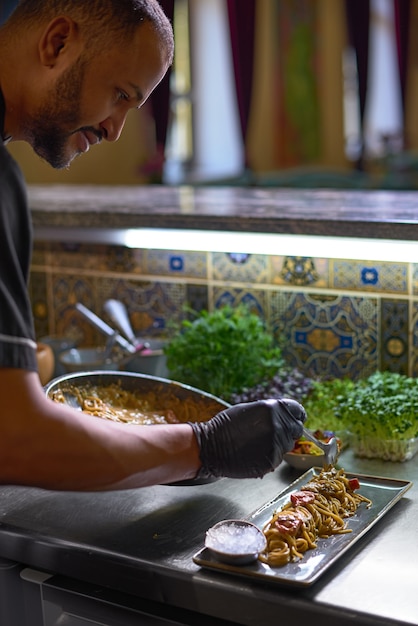 Lo chef mescola gli spaghetti in una padella i pomodori e le ostriche, piatto in un ristorante.