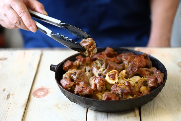 Lo chef mescola pezzi di carne fritta in una padella antiaderente. Spiedini di maiale in padella.