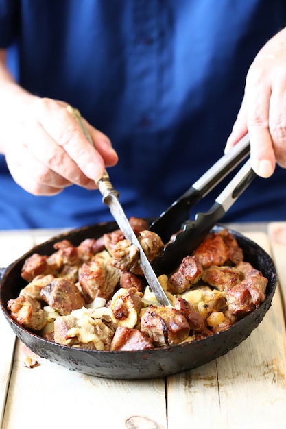 Lo chef mescola pezzi di carne fritta in una padella antiaderente. Spiedini di maiale in padella.