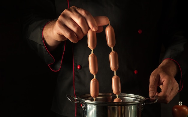 Lo chef mette le salsicce in una pentola bollente Cucina deliziosa colazione o cena in cucina