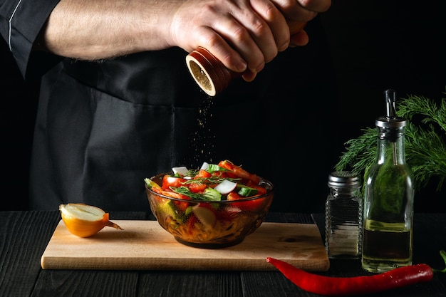 Lo chef nella cucina di un ristorante aggiunge i peperoni a un'insalata di verdure fresche