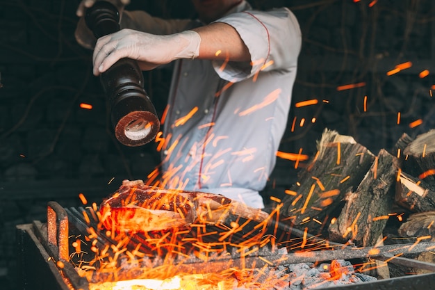 Lo chef pepa la bistecca sul fuoco.