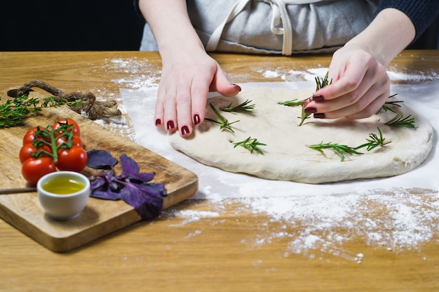 Lo chef prepara la focaccia, stende il rosmarino sull&#39;impasto.