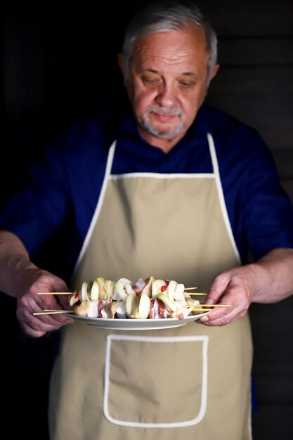 Lo chef prepara spiedini di pollo su bastoncini di legno