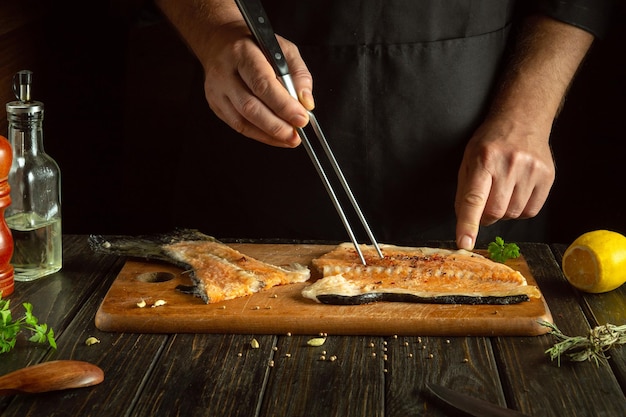 Lo chef prepara una bistecca di pesce fresco sul tavolo della cucina Il salmone è un pesce delizioso per preparare il pranzo o la colazione Forchetta in mano al cuoco