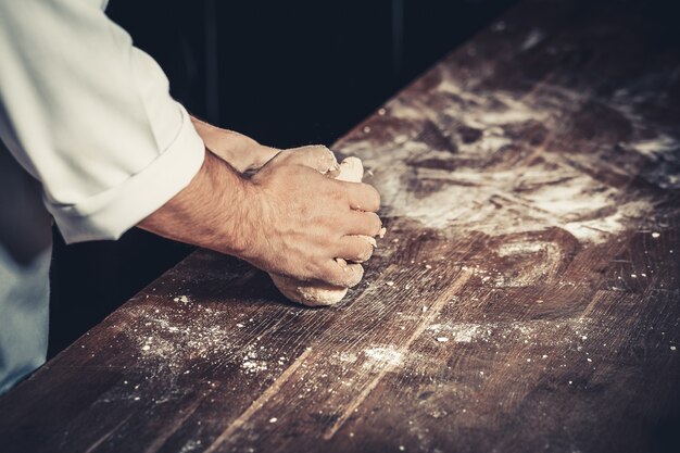 Lo chef professionista impasta l'impasto per pizza su un tavolo di legno. Farina in giro. Solo mani, da vicino